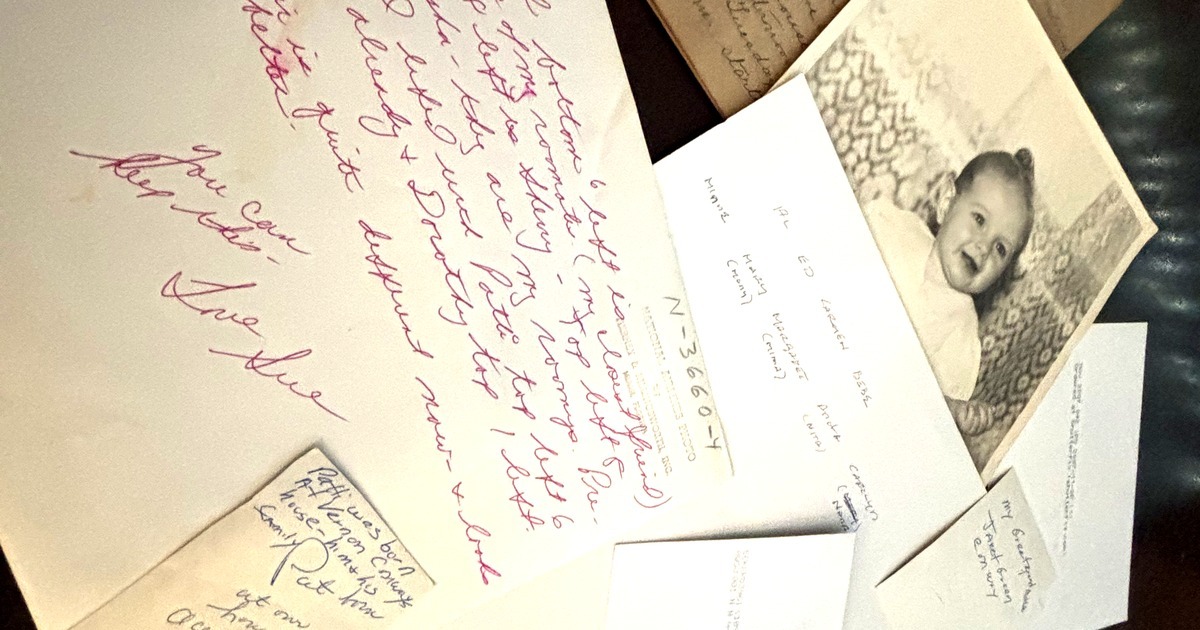 The backs of old family photos spread on a table: handwritten names and notes, a photographer's stamp, and one baby photo face up